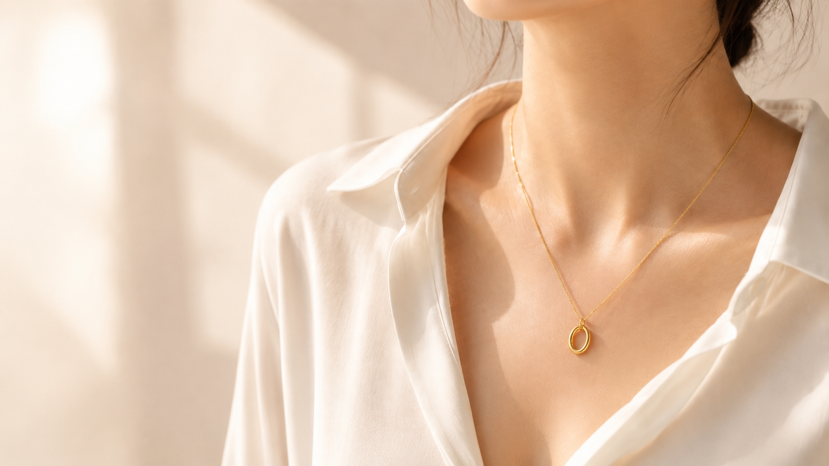 The Hollow Oval necklace worn close to the collarbone with a white shirt in warm light.